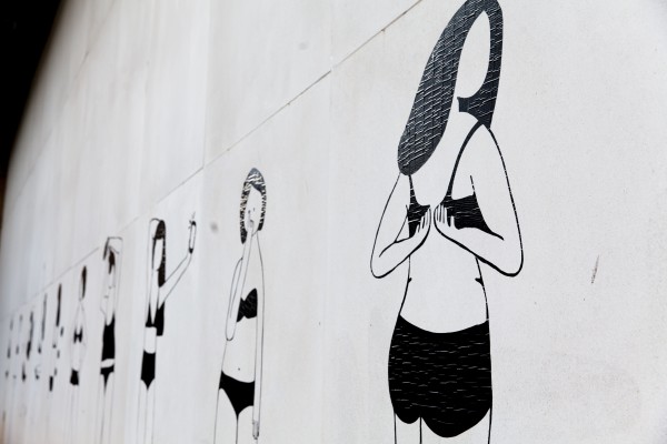 Detail of mural of 10 women in undergarments in various poses. Central women featured in photograph is clasping her bra. 