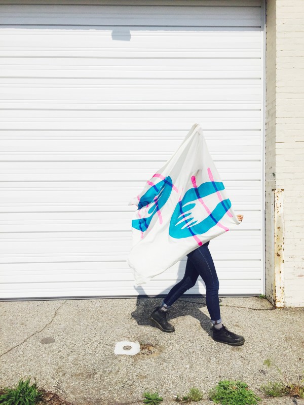 Model holding scarf that is blowing in wind. Design includes blue hands and pink lines. 