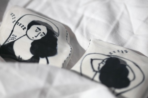 Two porcelain pillows painted with a girl sleeping on it photographed against white sheets. 