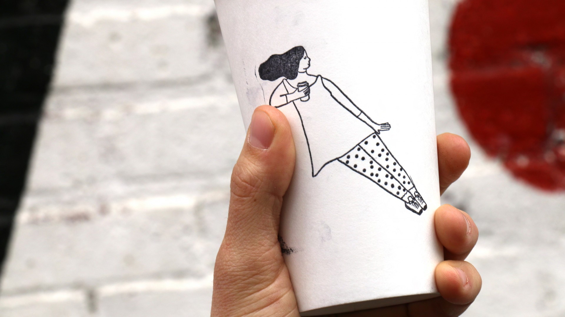 Hand holding up coffee cup with a stamped illustration of a tilted woman