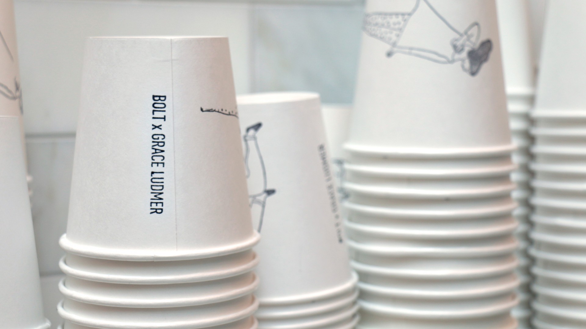 Close-up of stacks of coffee cups printed with illustrations and "Bolt x Grace Ludmer"
