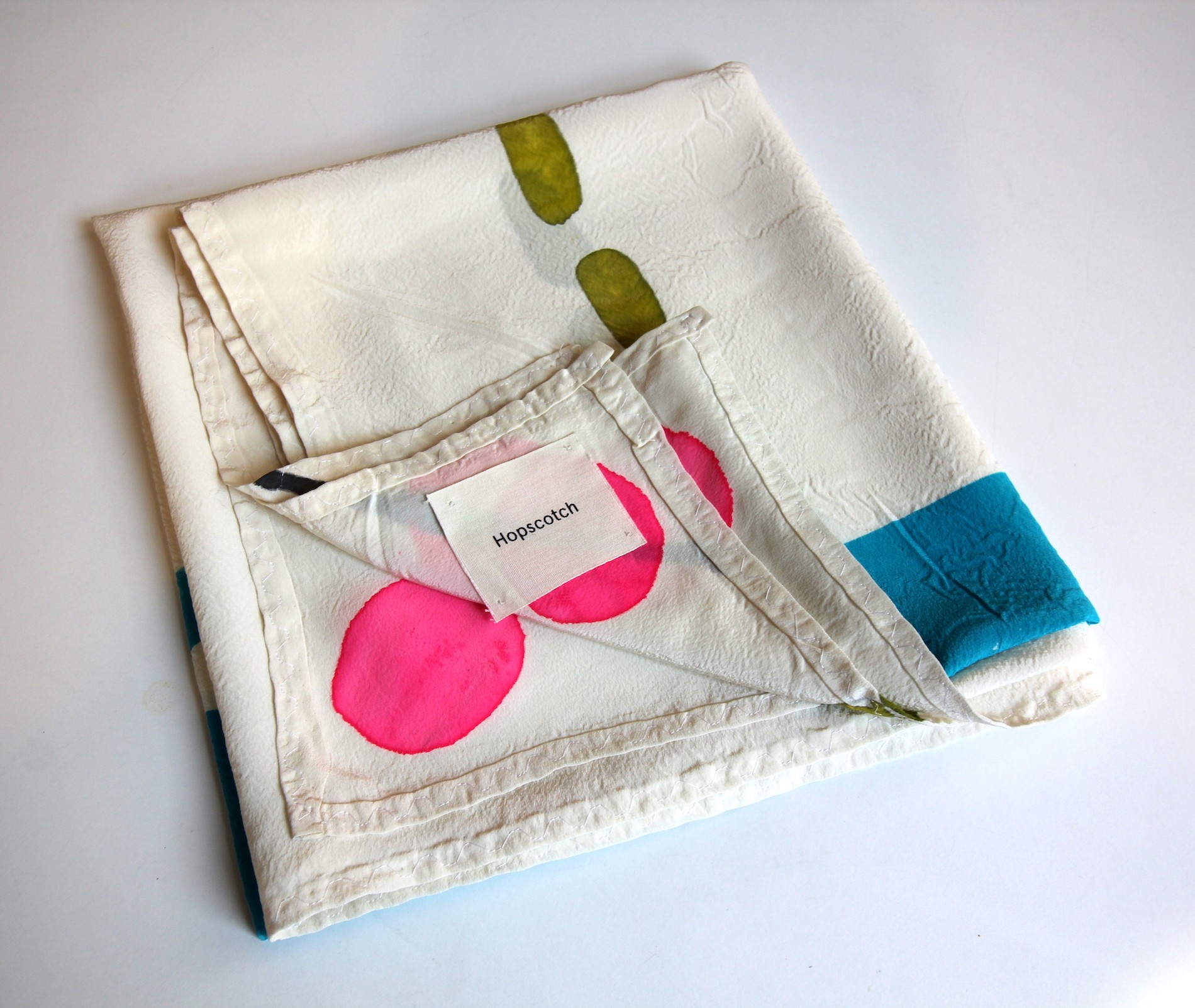 Scarf folded on white table showcasing tag that reads "Hopscotch"