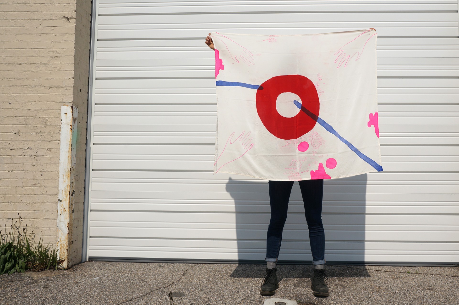 Model holding scarf against wall. Scarf design include bold red circle, pink squiggles and blue lines. 