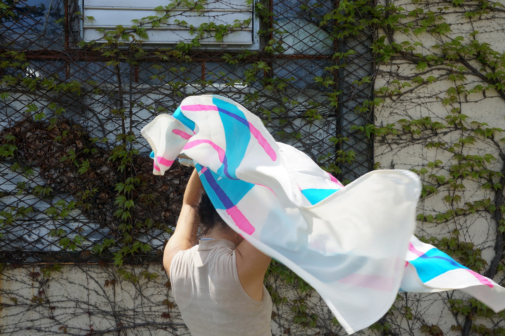 Model holding blue and pink scarf above head that is blowing in wind. 