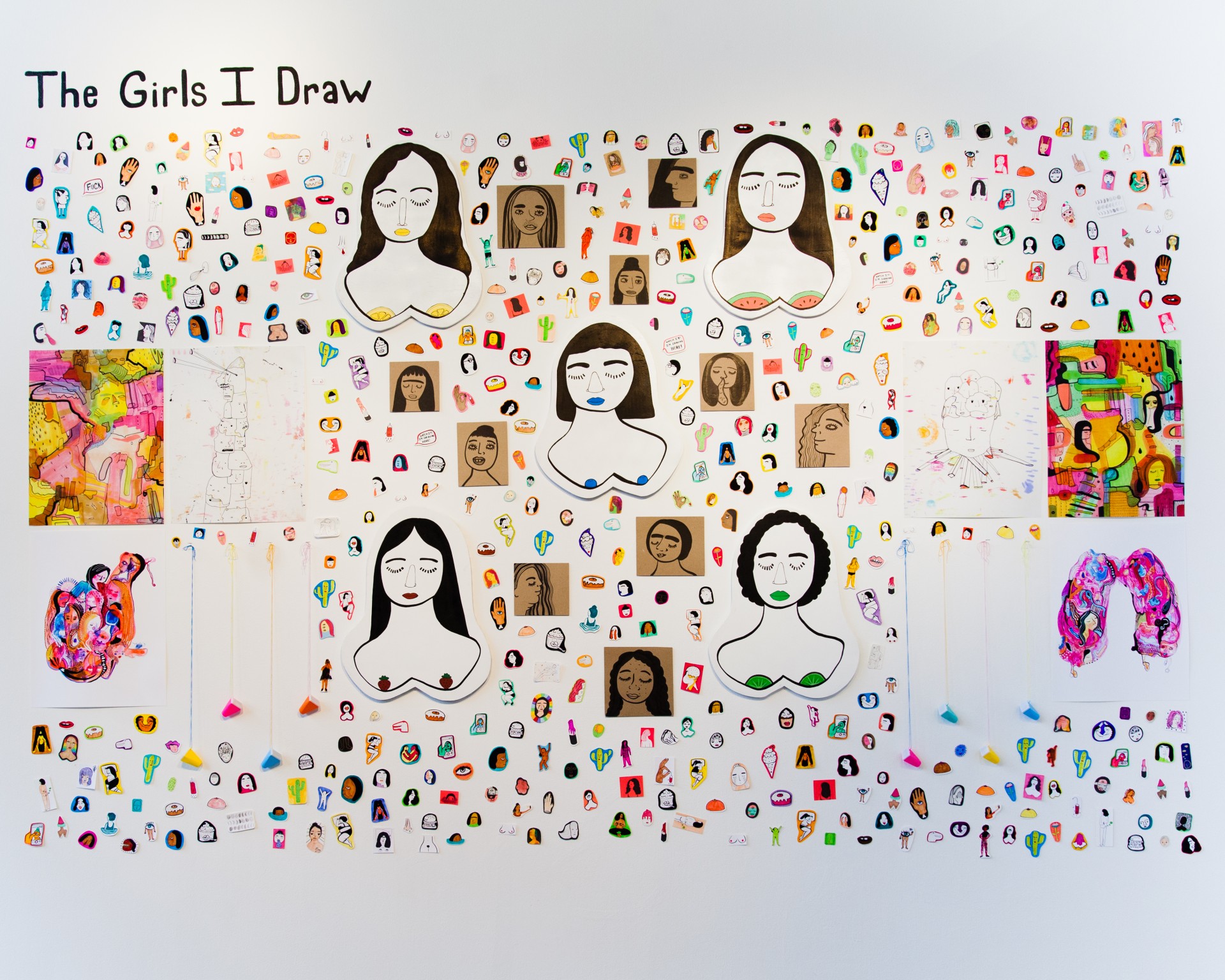White gallery wall with collaged assortment of stickers, paintings and drawings. 