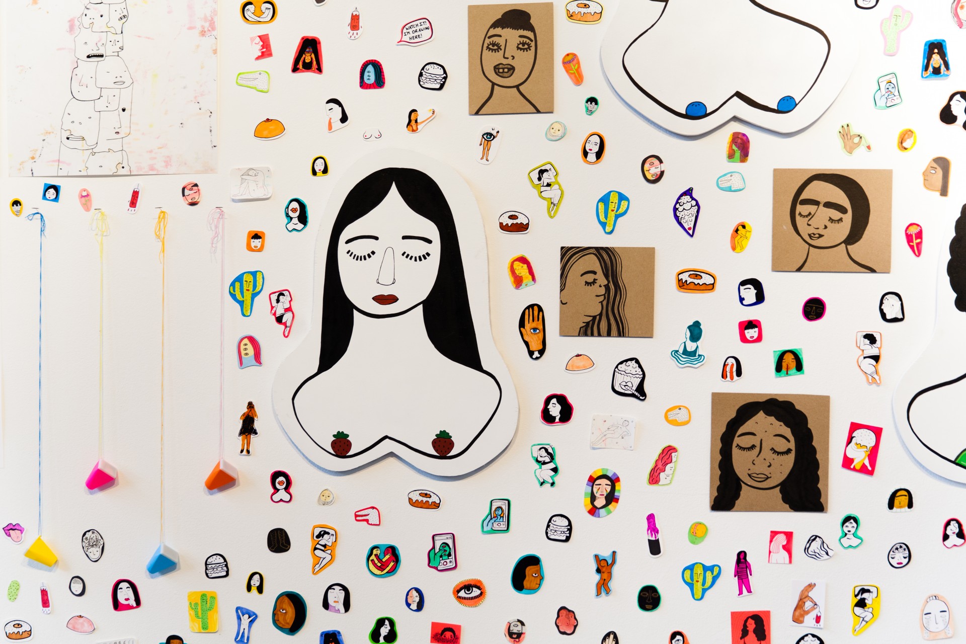 White gallery wall with collaged assortment of stickers, paintings and drawings. 