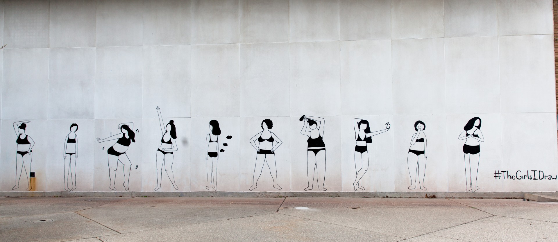 Photograph of wall with mural. Mural consists of 10 women in undergarments in various poses. Women are all rendered in black lines made out of duct tape.