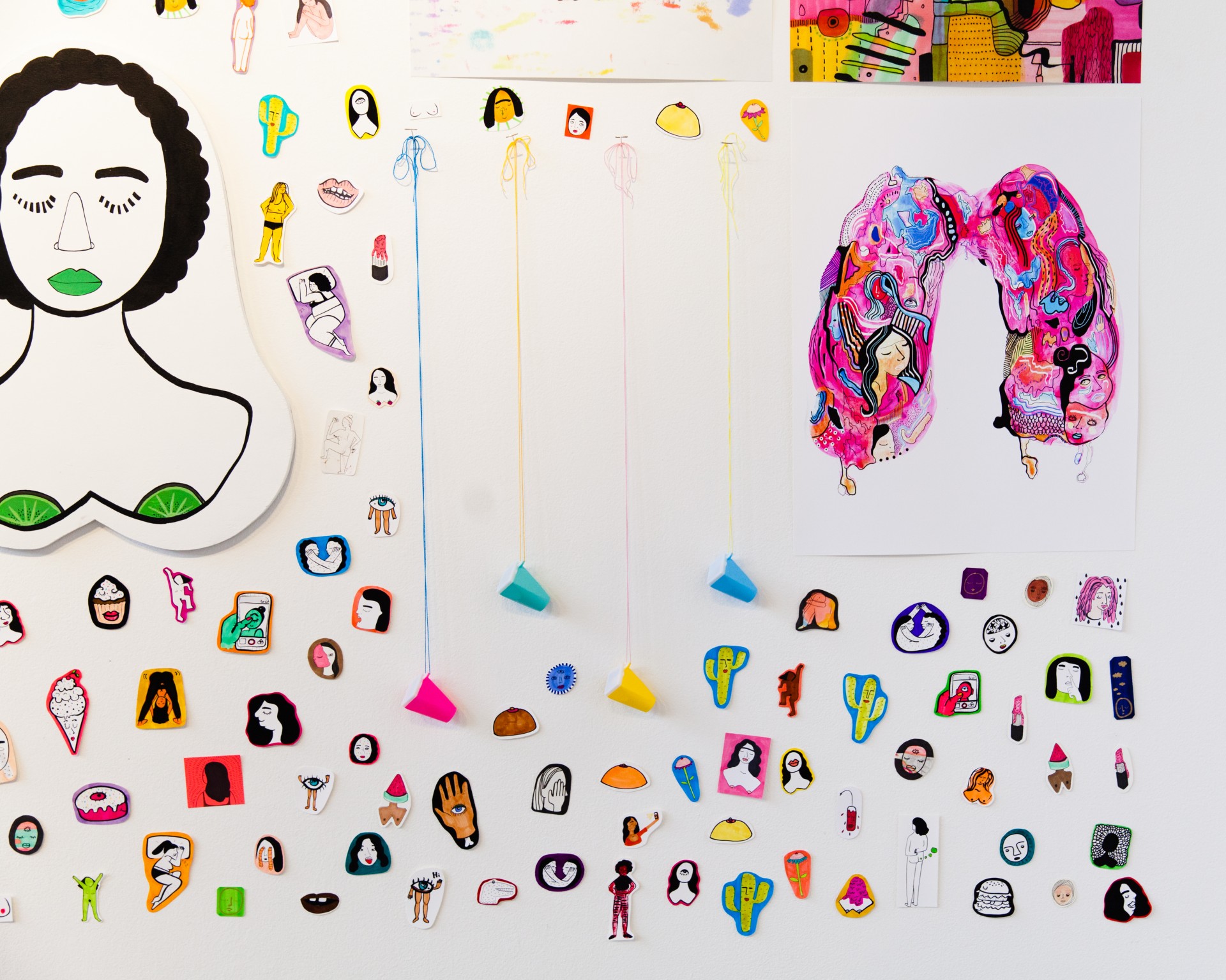 White gallery wall with collaged assortment of stickers, paintings and drawings. 