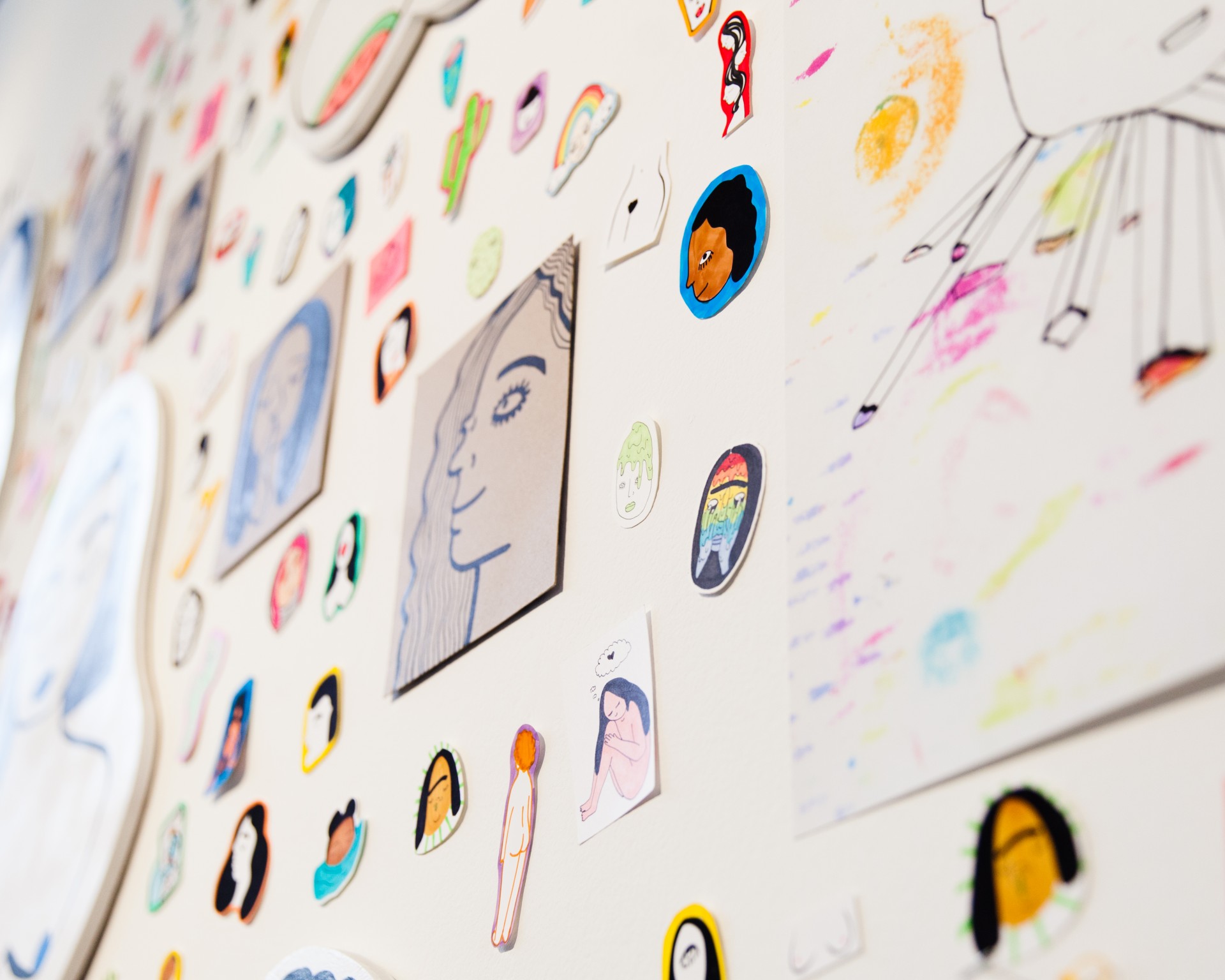 White gallery wall with collaged assortment of stickers, paintings and drawings. 