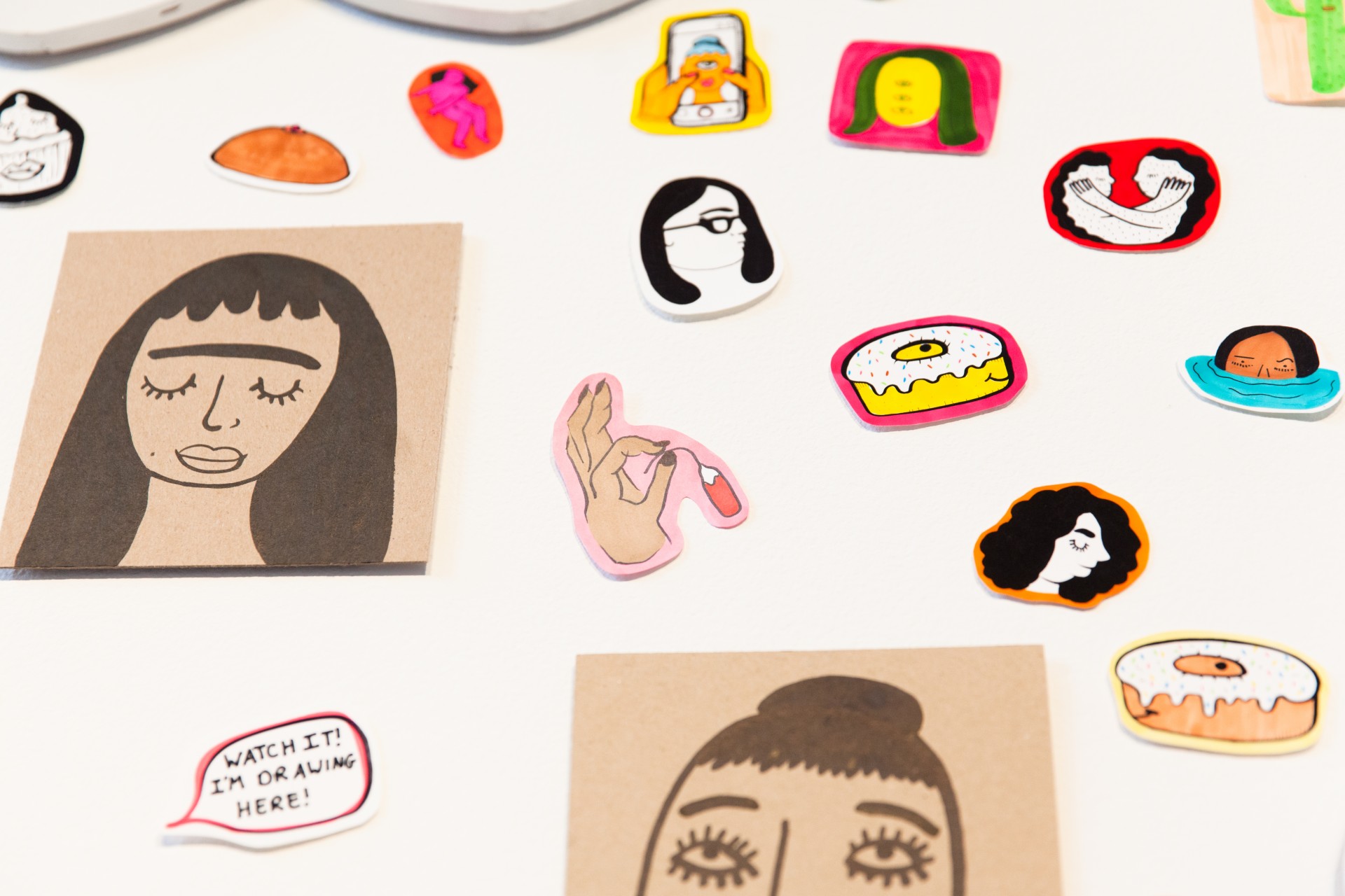 White gallery wall with collaged assortment of stickers, paintings and drawings. 