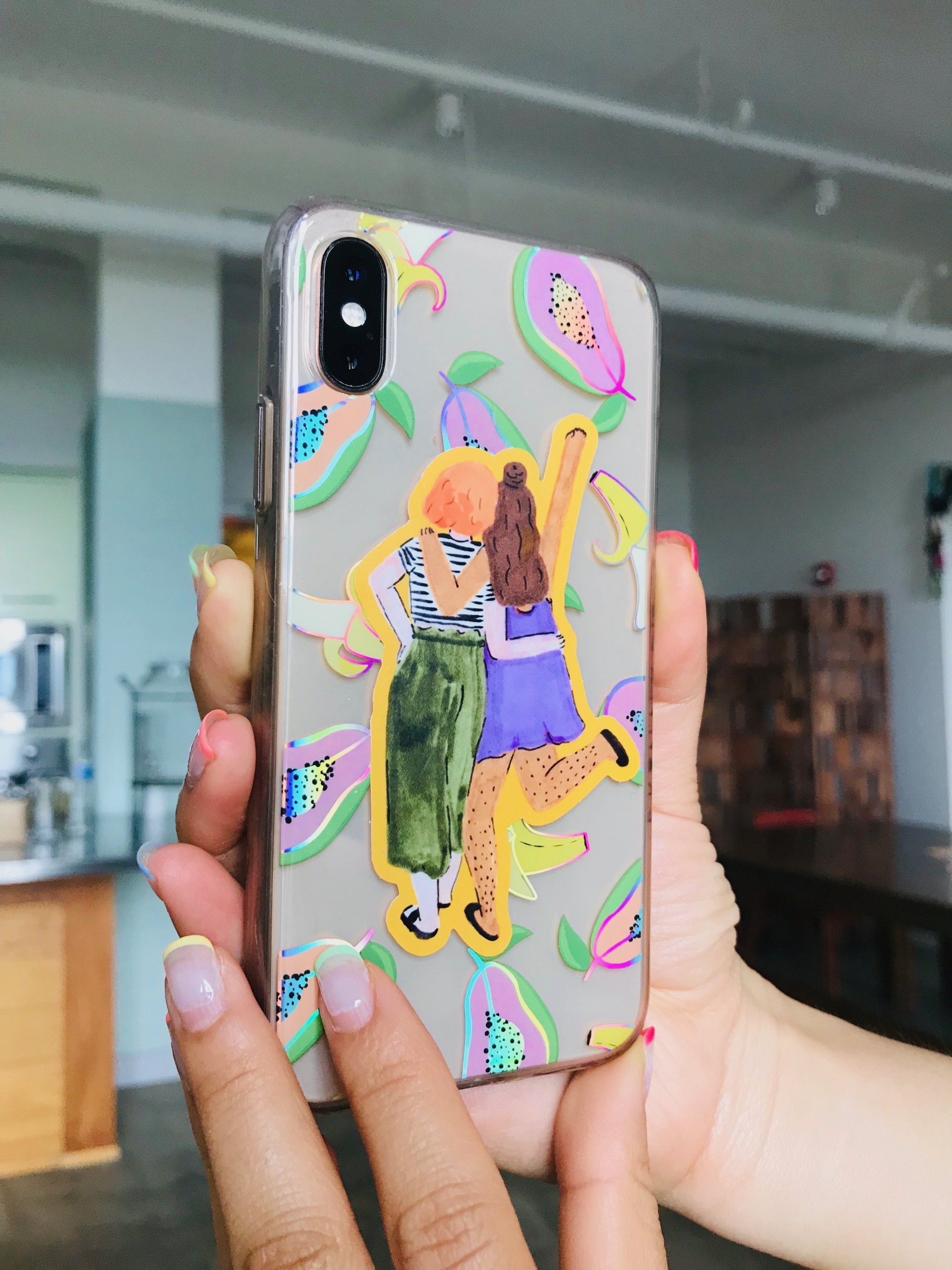 A sticker of two girls with their hands around each other with their back towards the viewer placed on an iphone