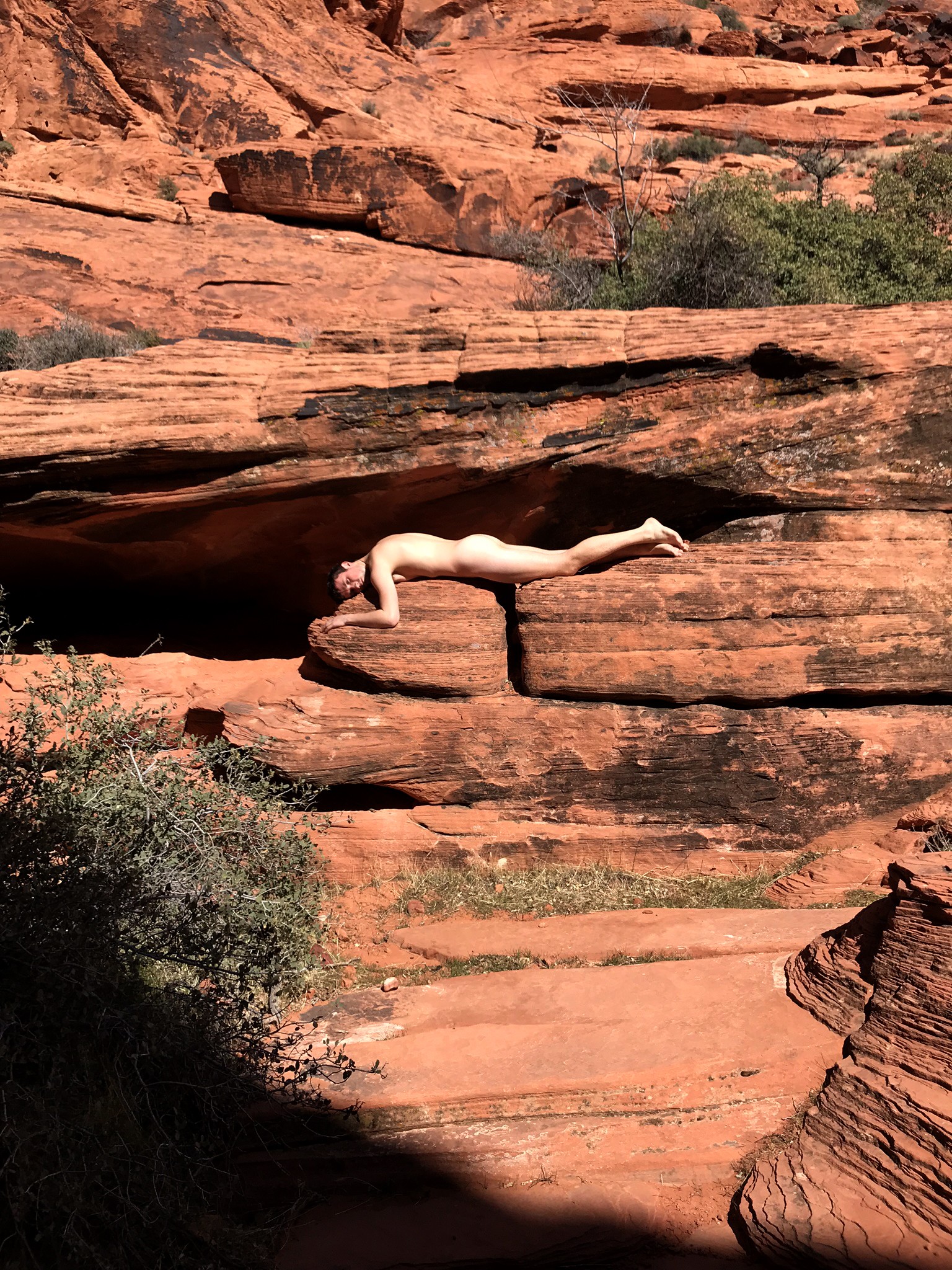Photograph of red rocks. Male model lays horizontal and nude in crevice of rock.