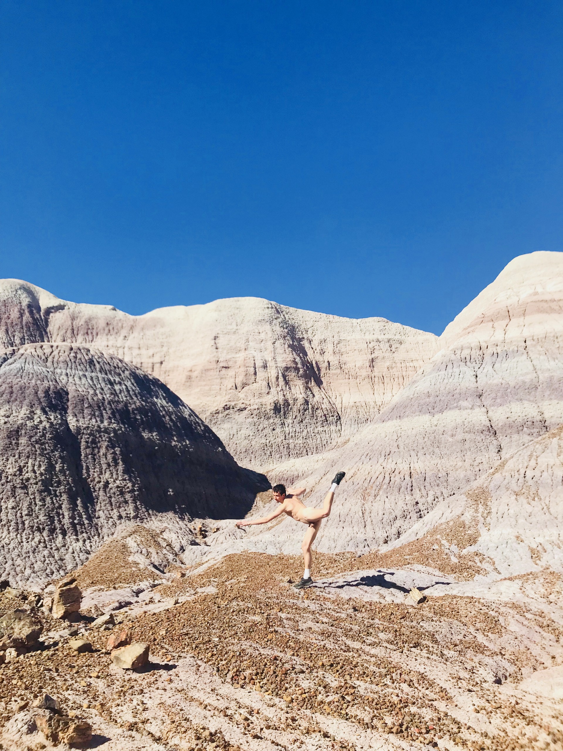 Photograph of Blue Mesa in Petrified Forrest in Arizona. Nude male model in center of image mid leap with leg in air.