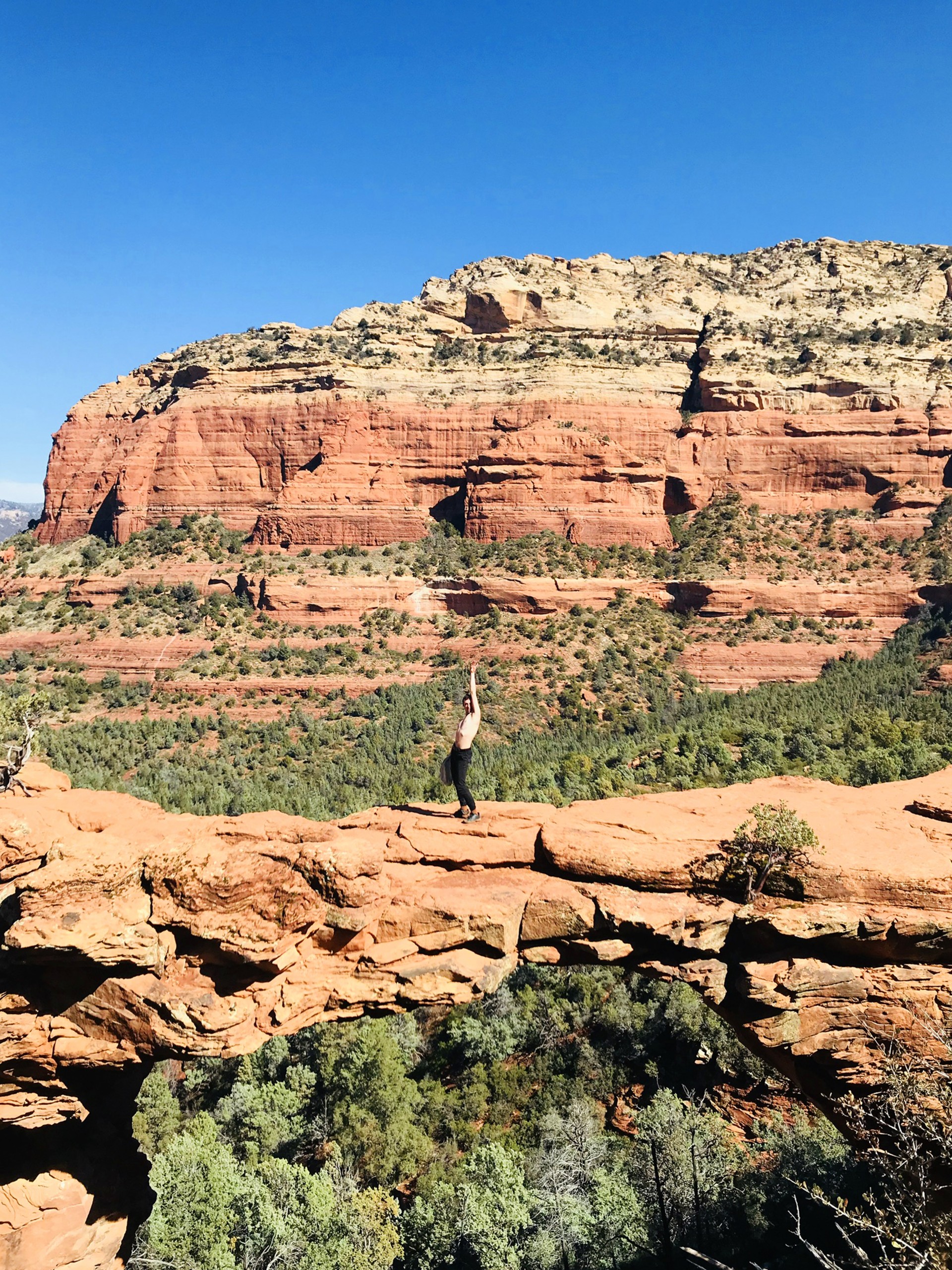 Photograph of Devil's Bridge in Sedona Arizona. Male model stands in center of bridge topless with hand draped above head. 