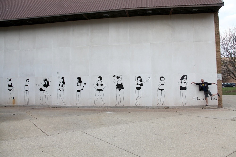 Photograph of wall with mural. Mural consists of 10 women in undergarments in various poses. Women are all rendered in black lines made out of duct tape. Single person poses to right side of mural.