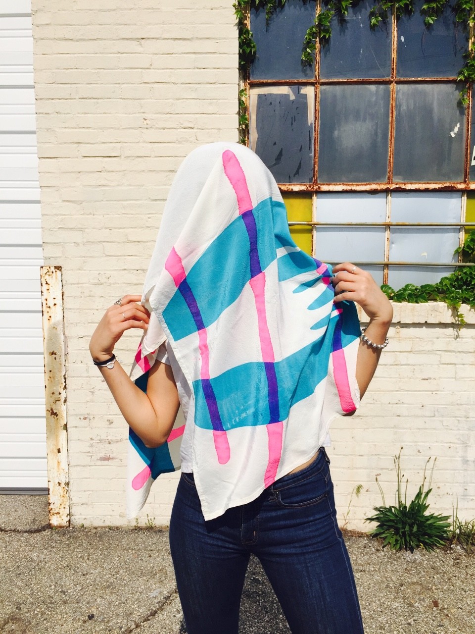 Scarf draped over head of model. Design includes blue hand and pink stripes. 