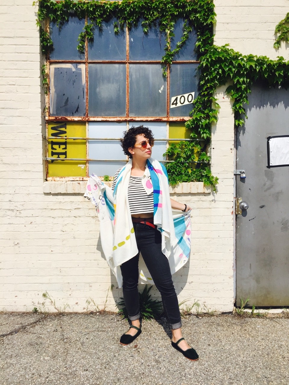 Model draped in scarves standing against window and ivy wall. 