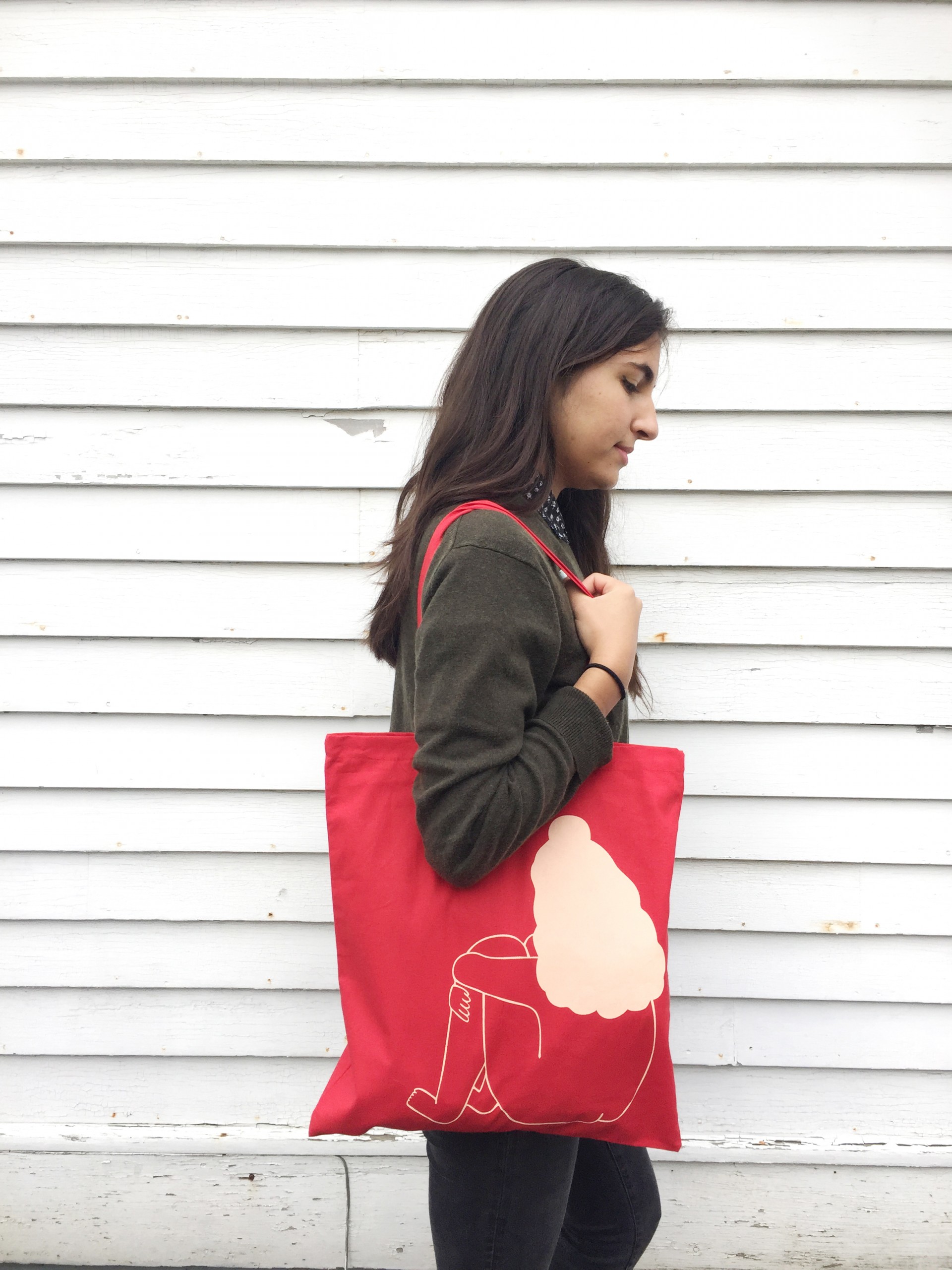 Red tote bag with a girl printed in light pink whose nude and sitting with her back facing viewer