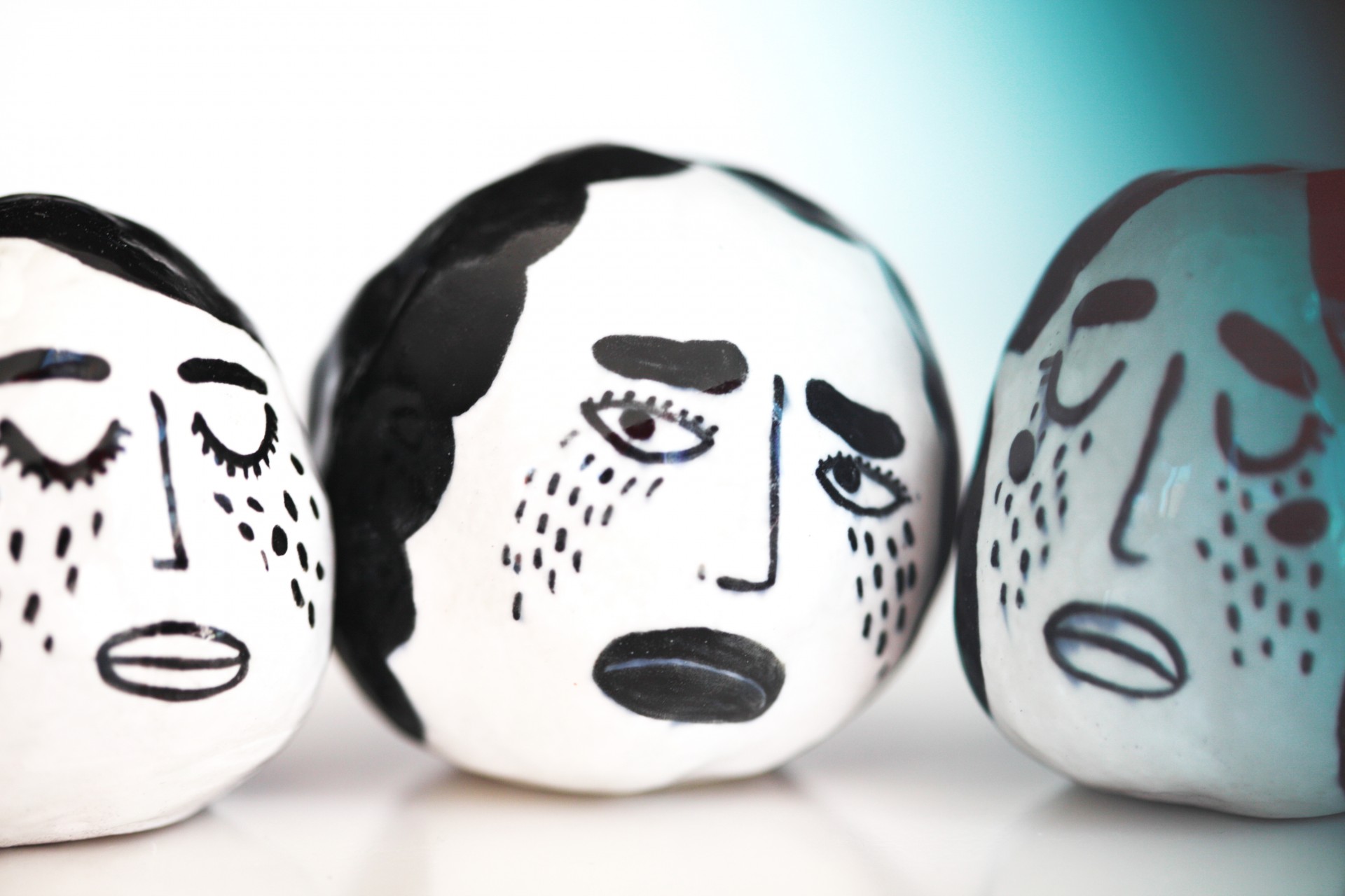 Three circular white porcelain rattles painted with black crying faces on white background. 