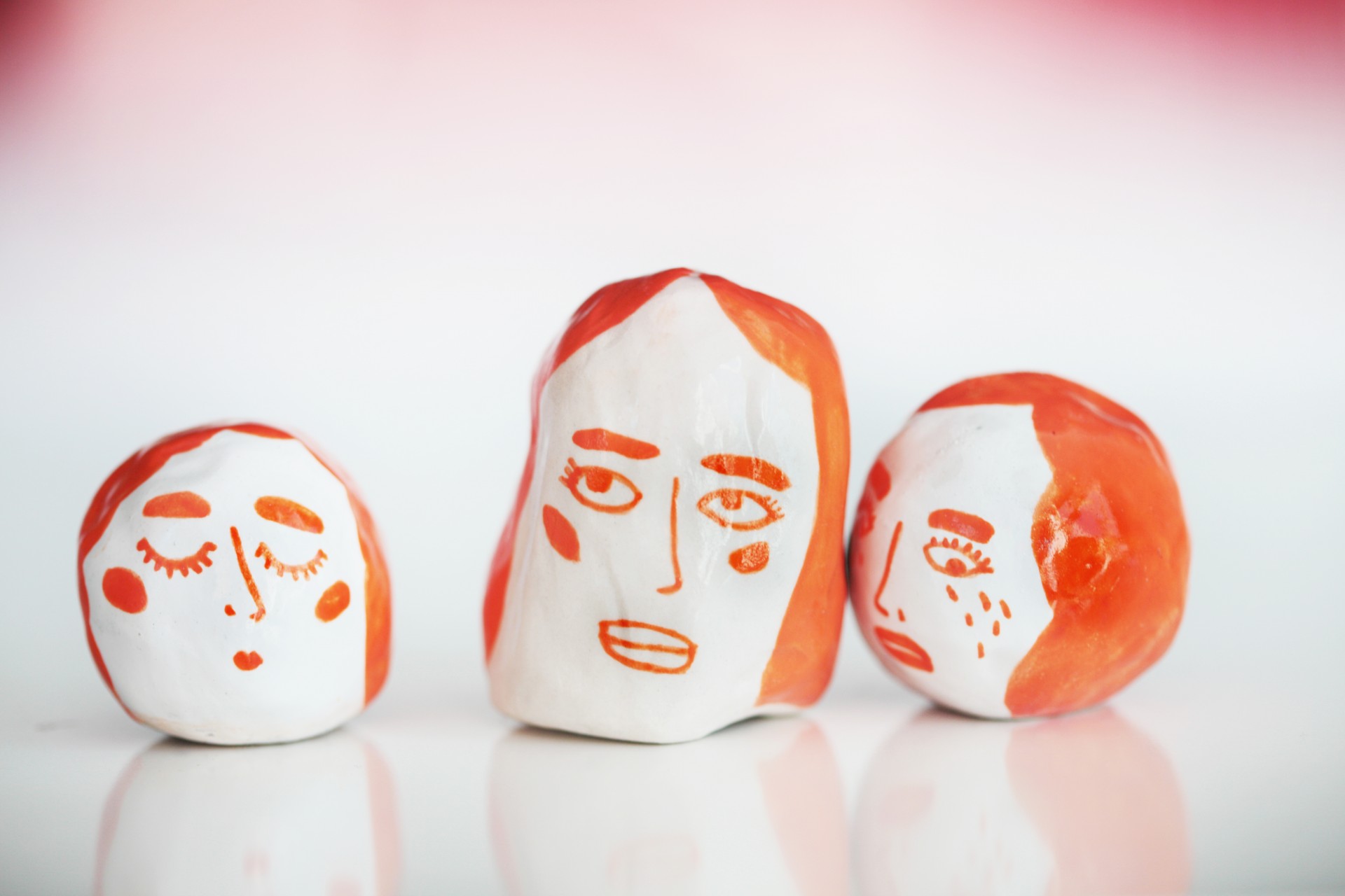 Three circular white porcelain rattles painted with orange faces on white background. 