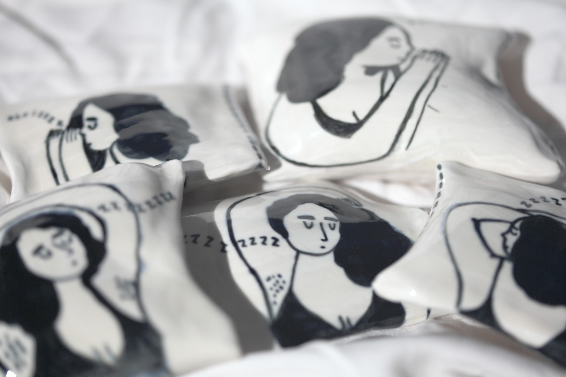 Collection of porcelain pillows painted girls sleeping photographed against white sheets. 