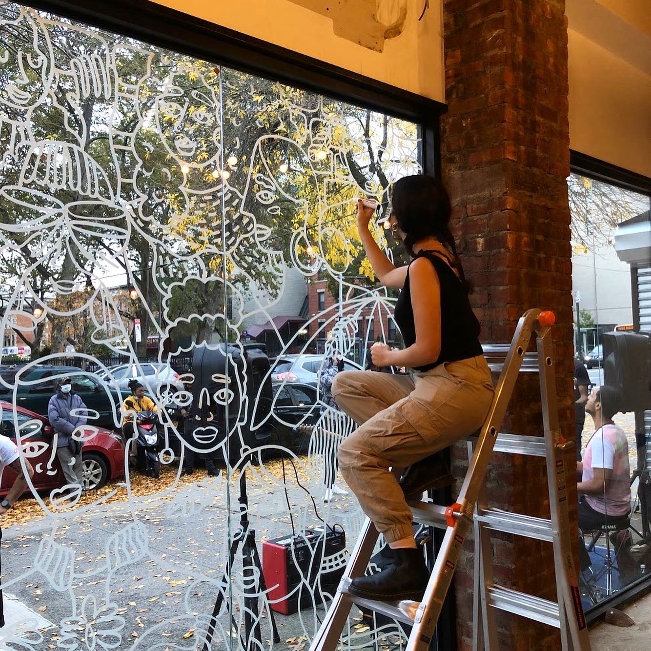 Grace sitting on ladder drawing on windows with chalk marker. 